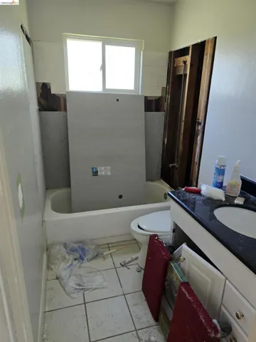 Bathroom featuring a white bathtub, a sliding window, and a vanity with a dark countertop and integrated sink