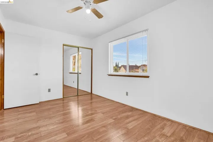 Room featuring wood-finish flooring, a window with horizontal blinds, and a ceiling fan with integrated lighting