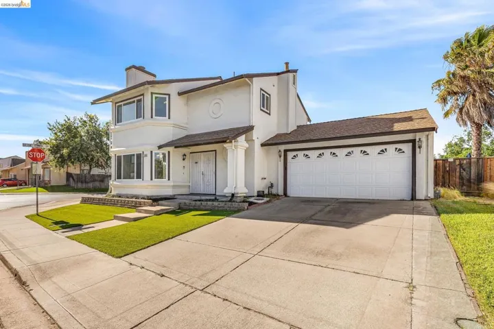 Two-story stucco home featuring a two-car garage with decorative window inserts, an expansive concrete driveway, and a covered entry porch supported by white columns