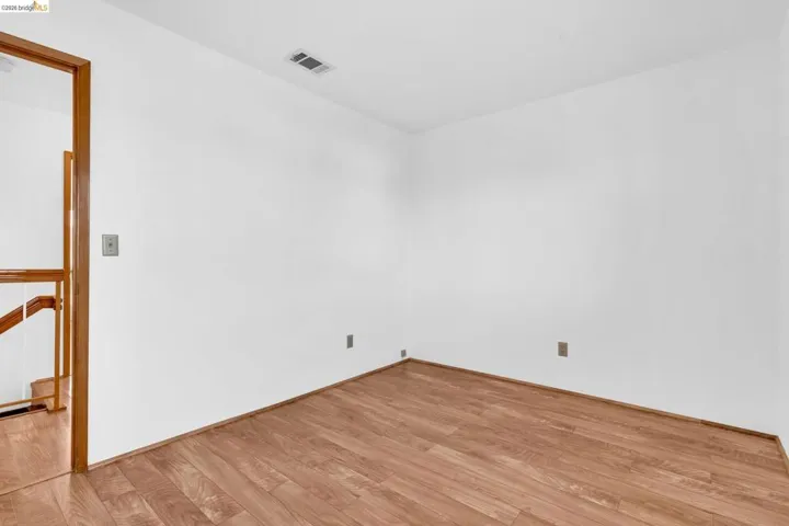 Room featuring wood-finish flooring, white walls, and a light-toned wooden door frame