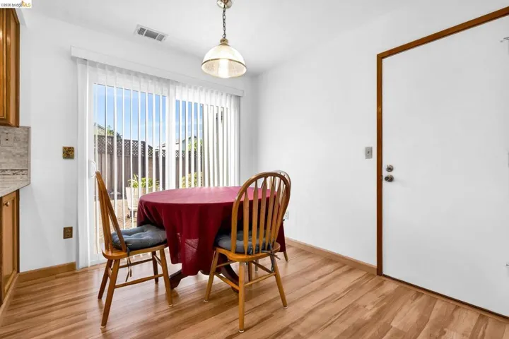 Dining area featuring wood-finish flooring, white walls, and a glass sliding door with vertical blinds