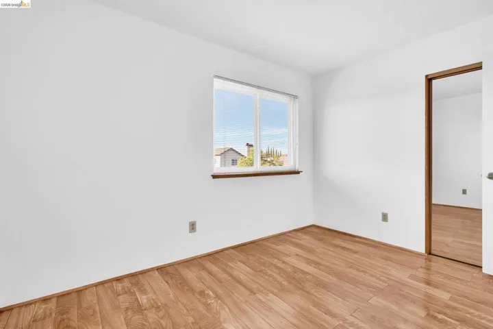 Bright room featuring wood-finish flooring, a double-paned window with blinds, and a built-in closet with mirrored sliding doors