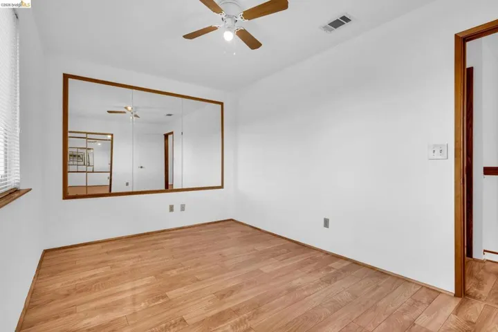 Room featuring wood-finish flooring, white walls, and a wood-trimmed mirror