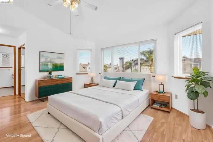 Bright room featuring multiple windows, wood-finish flooring, a ceiling fan, and white walls