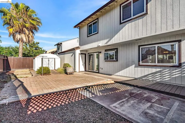 Rear exterior featuring a brick paver patio, a concrete pad, and a wooden deck