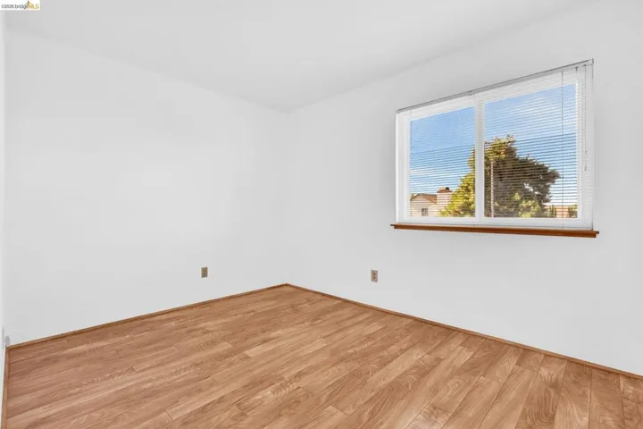 Bright interior space featuring a window with integrated blinds, white wall finishes, and wood-finish flooring
