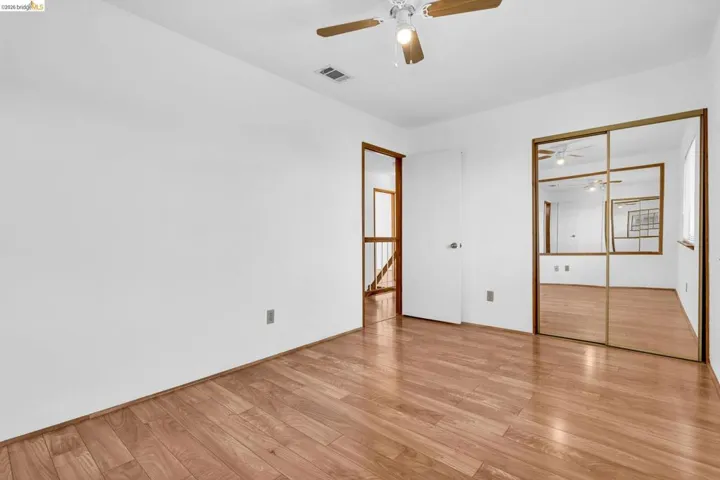 Spacious room featuring wood-finish flooring, a ceiling fan with integrated lighting, and mirrored closet doors with gold-tone framing