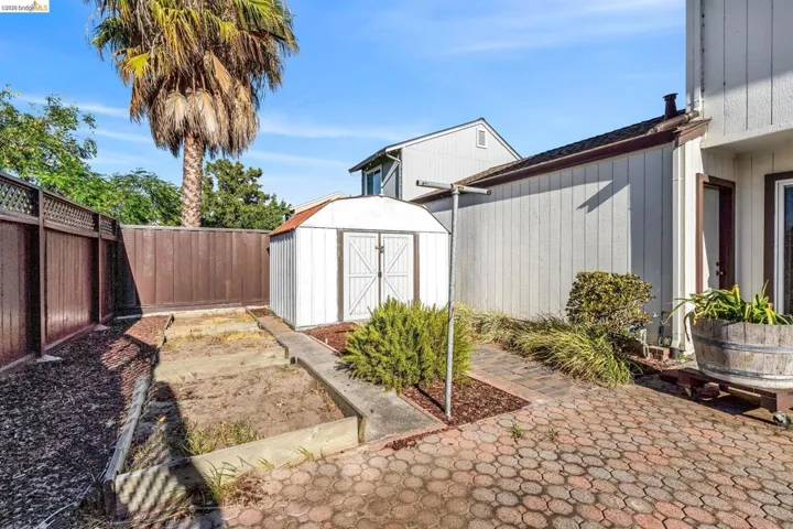 Private backyard space featuring a white storage shed, paver patio, wood fencing, and raised garden beds