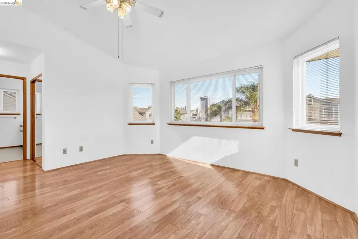 Spacious room featuring wood-finish flooring, multiple windows with blinds, a ceiling fan with integrated lighting, and white walls