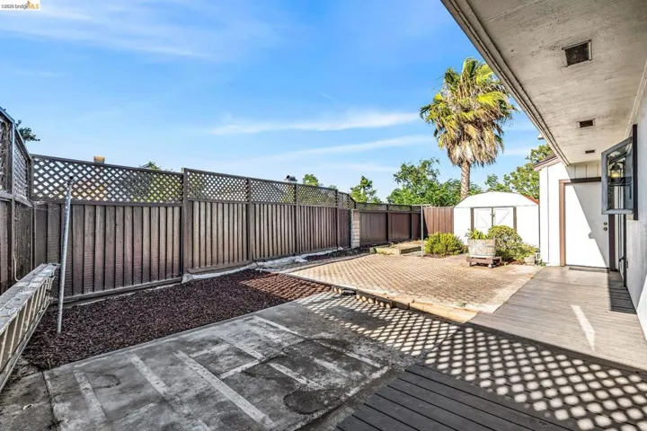 Private outdoor space featuring a wood-finish deck, concrete patio, and a storage shed