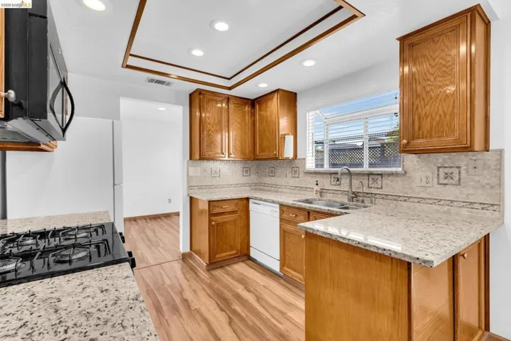 Kitchen featuring wood-finish cabinetry, light-toned granite countertops, a tiled backsplash, wood-finish flooring, and recessed lighting