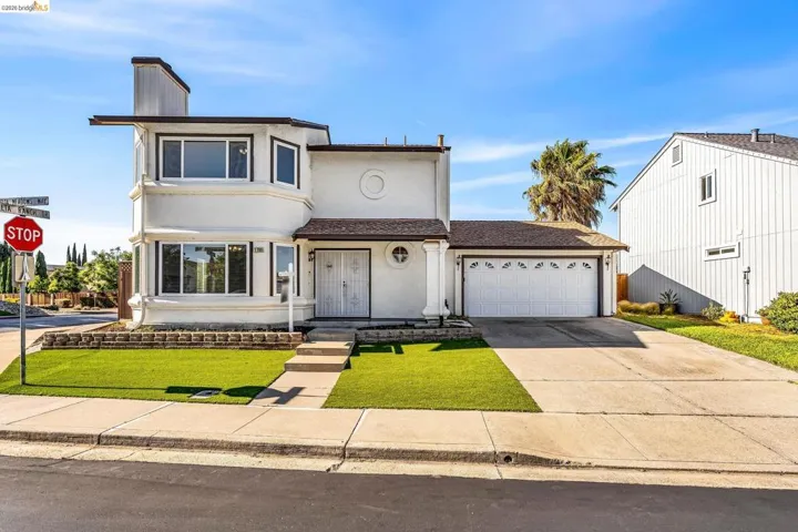 Two-story stucco residence featuring a two-car garage, mature palm tree, and a concrete driveway