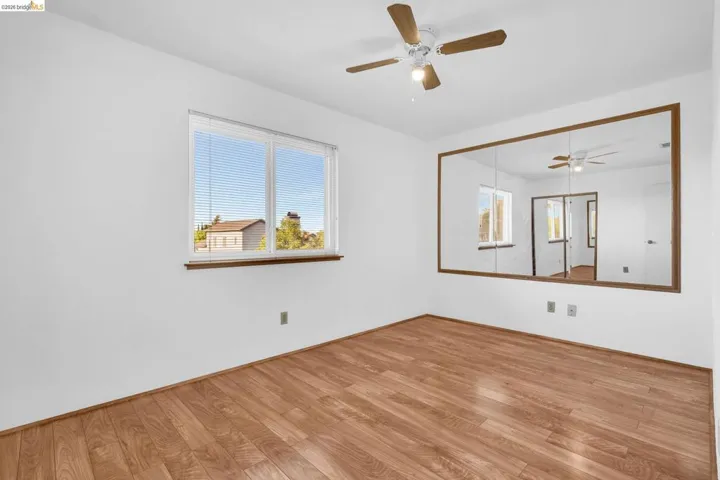 Room featuring wood-finish flooring, a ceiling fan with integrated lighting, and a large window with horizontal blinds