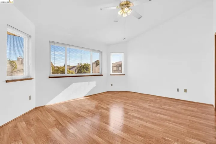 Spacious interior featuring wood-finish flooring, white walls, multiple windows, and a ceiling fan