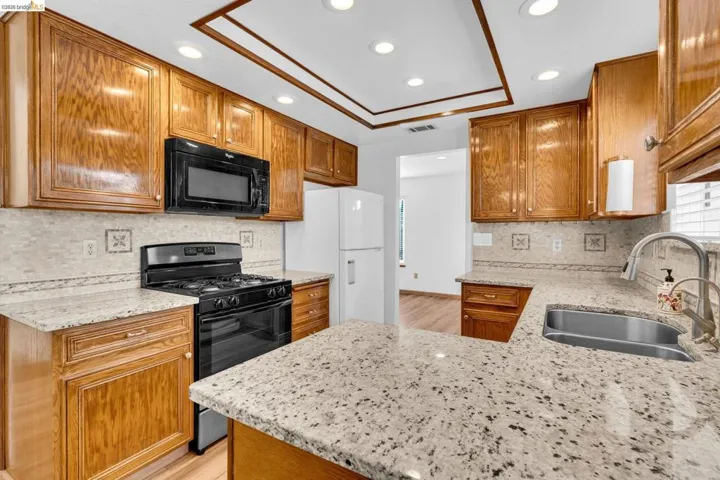 Kitchen featuring wood cabinetry, light speckled countertops, a tile backsplash, and recessed ceiling lighting