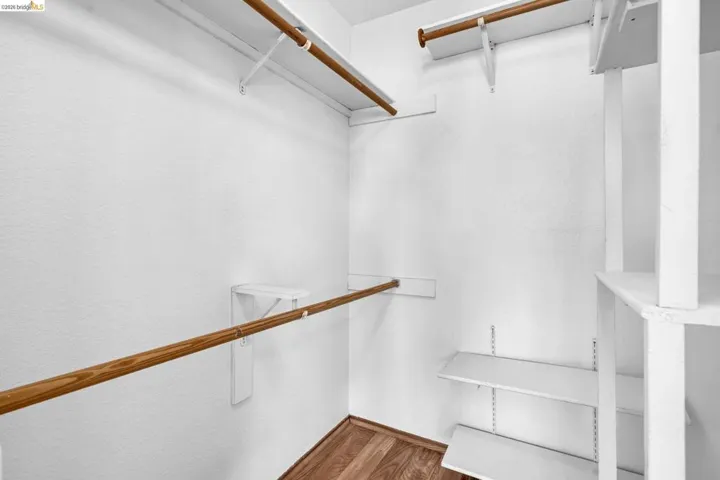 Walk-in closet featuring white walls, wood-finish flooring, multiple wood hanging rods, and adjustable white shelving units
