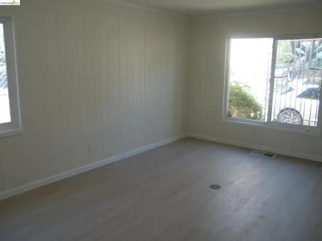 Spacious room featuring wood-finish flooring, vertical paneling, white baseboards, and two windows
