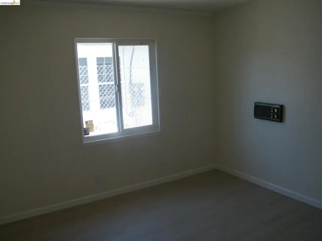 Light-filled interior space featuring a sliding window with security bars, wood-finish flooring, white baseboards, and a wall-mounted intercom system