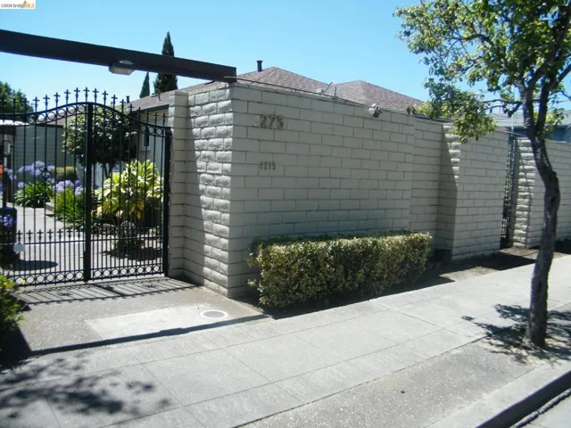 Gated entry featuring a wrought iron gate, stone block wall, and mature landscaping