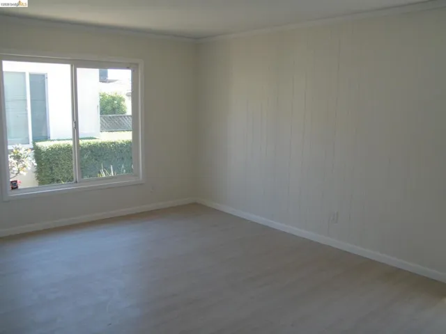 Bright interior room featuring a large sliding window, white wall paneling, and wood-finish flooring