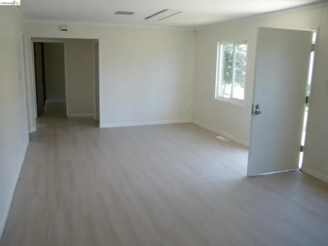 Spacious room with wood-finish flooring, white baseboards, and crown molding