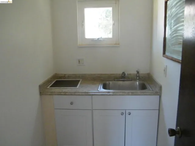 Kitchenette featuring a built-in electric stovetop, stainless steel sink, light-toned countertop, white cabinetry, and a window for natural light
