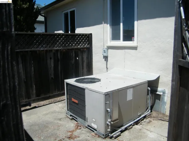 Outdoor concrete patio area featuring a climate control unit and a wooden privacy fence with an open lattice top