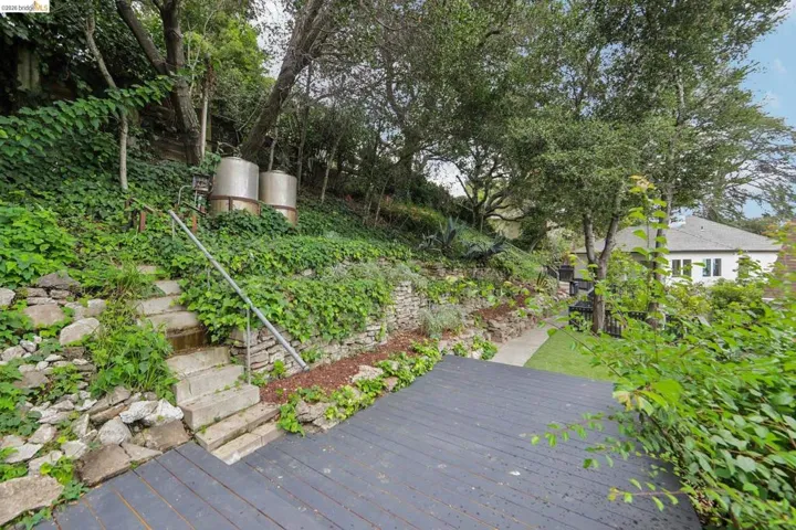 Expansive terraced yard featuring a dark-toned deck, stone retaining walls, and mature trees