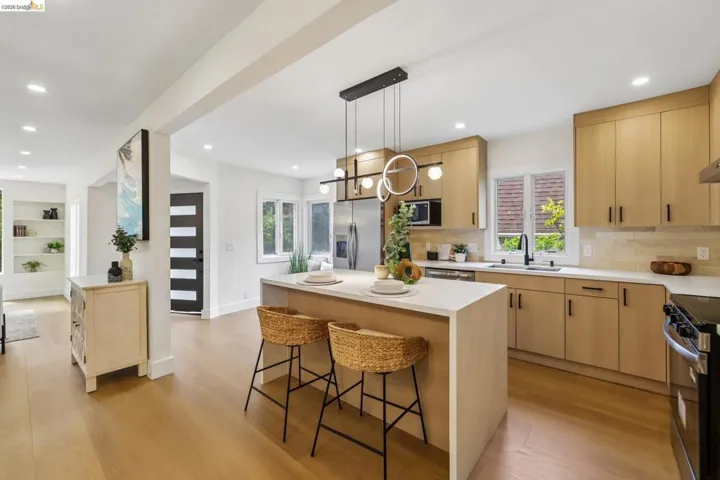 Contemporary kitchen featuring light wood-finish cabinetry, white countertops, and a central island with integrated seating