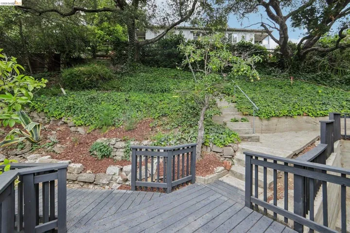 Multi-level outdoor deck featuring dark-painted wood railings and steps leading to an upper paved area with handrails