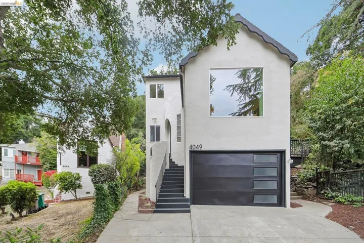 Stucco exterior with a peaked roofline, featuring a large square picture window, a contemporary black garage door with frosted glass panels, and an arched entry with exterior sconce lighting