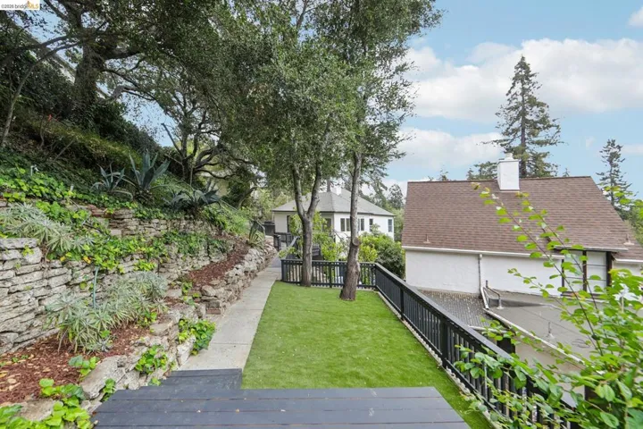 Expansive exterior space featuring a manicured lawn area, stone retaining walls with plantings, and mature trees