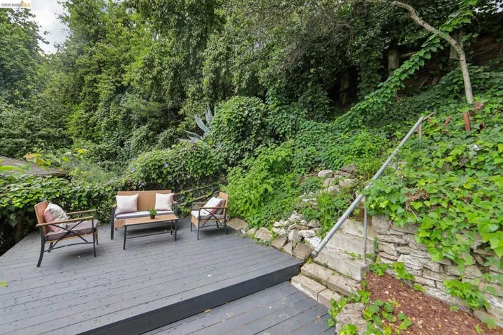 Spacious outdoor deck featuring gray wood-finish decking, surrounded by lush green foliage