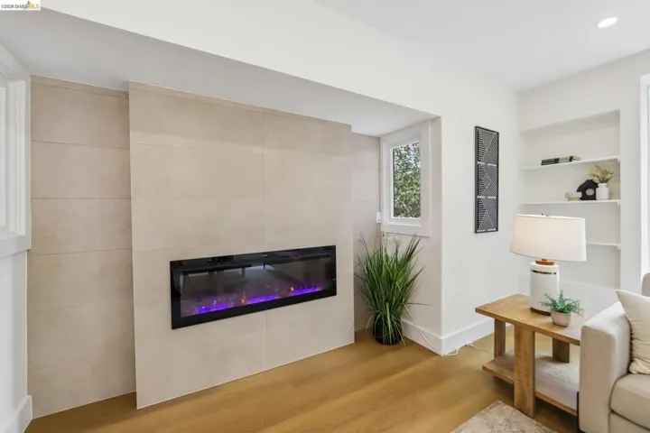 Integrated electric fireplace with tiled surround, vinyl plank flooring, built-in shelving, white trim, and recessed lighting