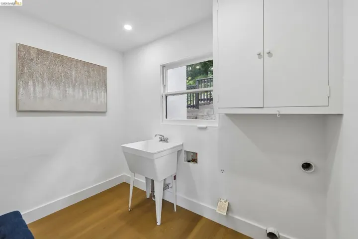 Laundry room featuring a built-in wash sink with a chrome faucet, white wall cabinetry, a window, vinyl plank flooring.