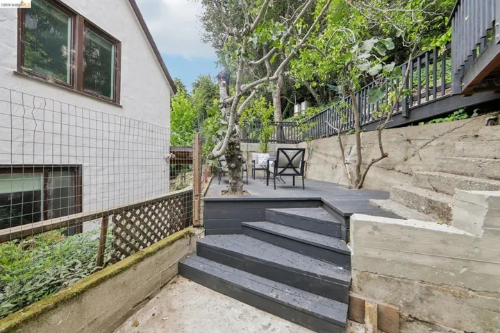 Multi-level outdoor living space featuring a dark-stained wood deck with stairs, concrete retaining walls, and established trees