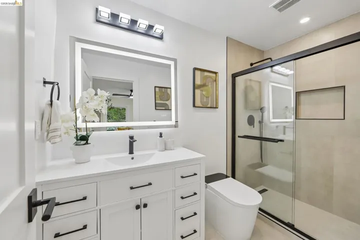 Contemporary bathroom featuring a white vanity with integrated sink, black matte fixtures, and an illuminated mirror