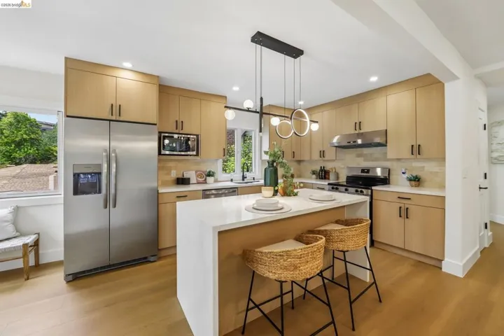 Open-concept kitchen featuring wood-finish cabinetry, stainless steel appliances, a center island with a light-toned countertop, and modern pendant lighting