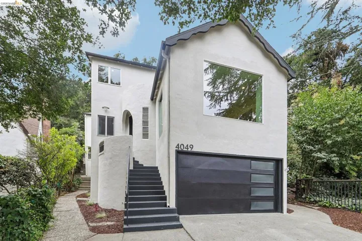 Contemporary stucco exterior featuring a striking black garage door with frosted glass panels, a prominent large square window, and a separate entrance with a curved stucco staircase