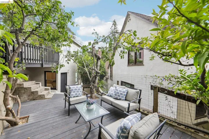 Spacious outdoor deck featuring gray wood-finish flooring, mature trees, concrete steps, and a black railing
