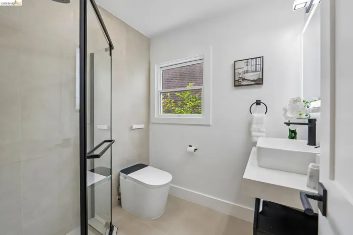 Modern bathroom featuring a walk-in shower with black-framed glass enclosure, light-toned wall tile, and a contemporary toilet