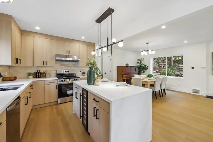 Modern kitchen featuring light wood-finish cabinetry, stainless steel appliances, and an expansive island with a built-in beverage cooler