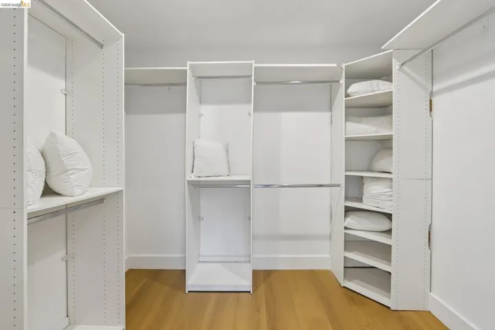 Custom closet system featuring white built-in shelving, chrome hanging rods, and vinyl plank flooring