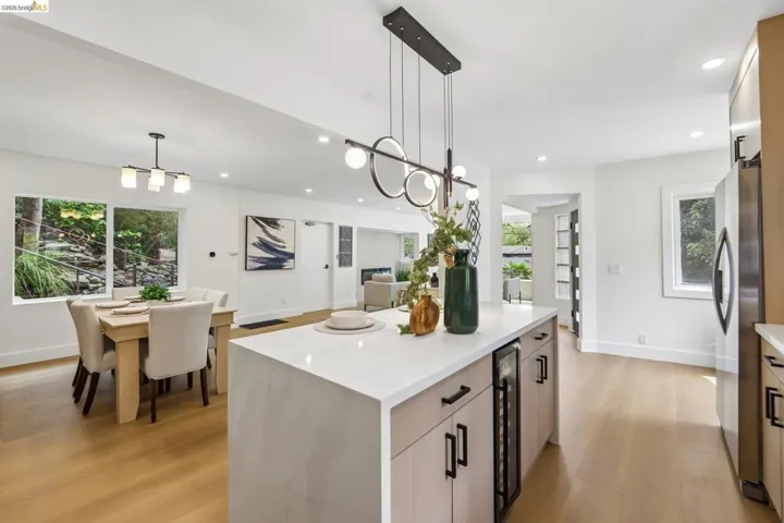 Open-concept kitchen and dining area featuring a central island with a built-in beverage refrigerator, vinyl plank flooring, recessed lighting, and a modern linear chandelier