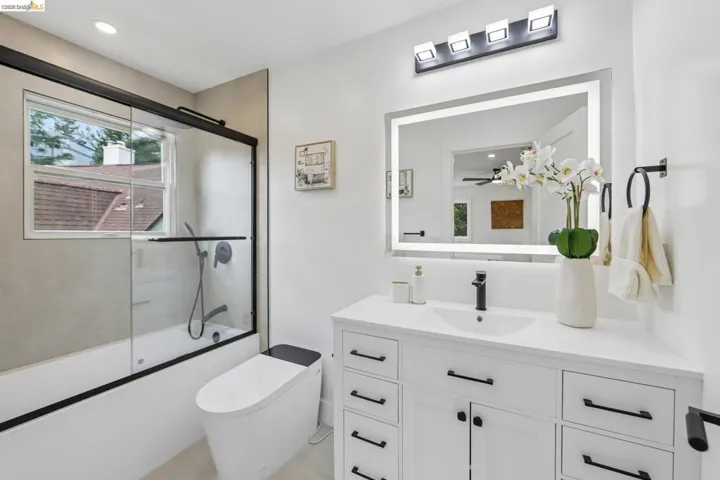 Contemporary bathroom featuring a white vanity with extensive storage, a large illuminated mirror, and a sleek matte black faucet