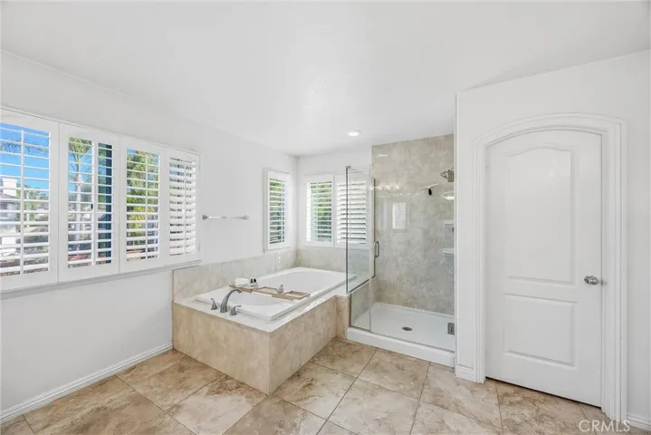 Spacious primary bathroom featuring a soaking tub, separate glass-enclosed shower, and plantation shutters.