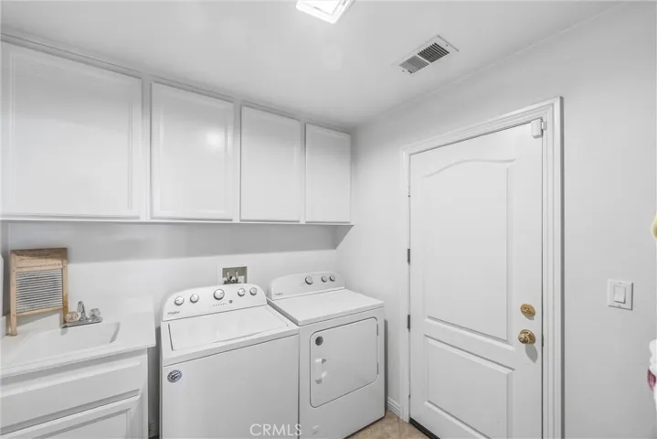Convenient laundry room with a utility sink, overhead cabinets, and additional storage space.