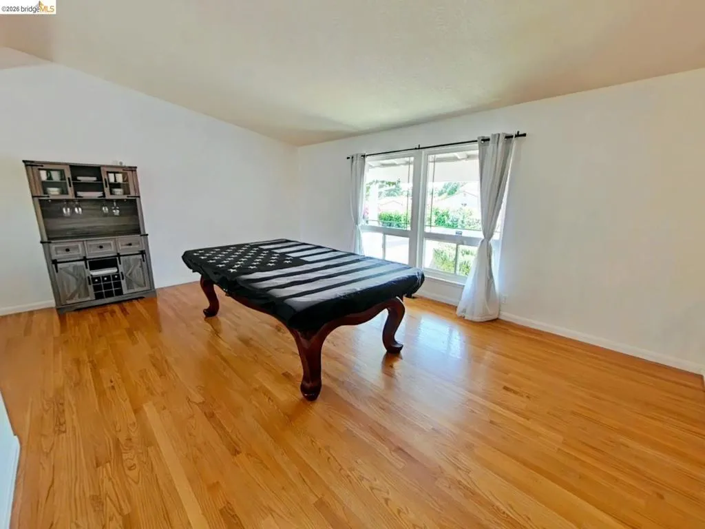 Spacious room featuring wood-finish flooring, white walls, and large windows with natural light