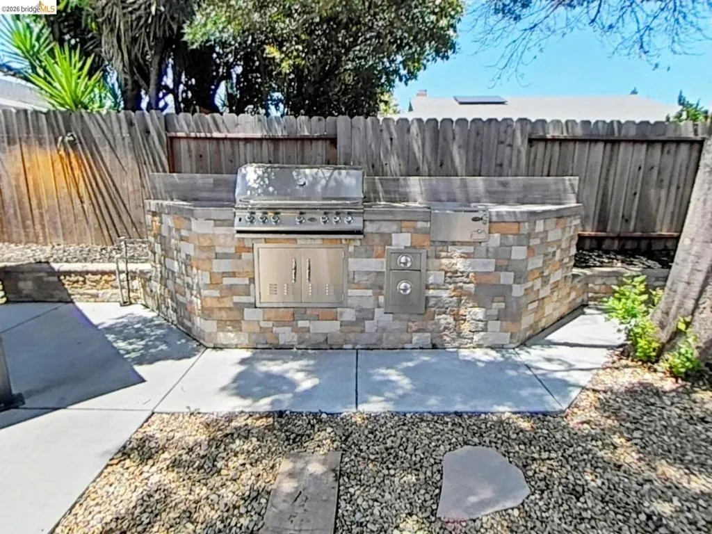 Outdoor kitchen featuring a stone veneer island with a built-in grill, stainless steel cabinetry, and concrete countertops