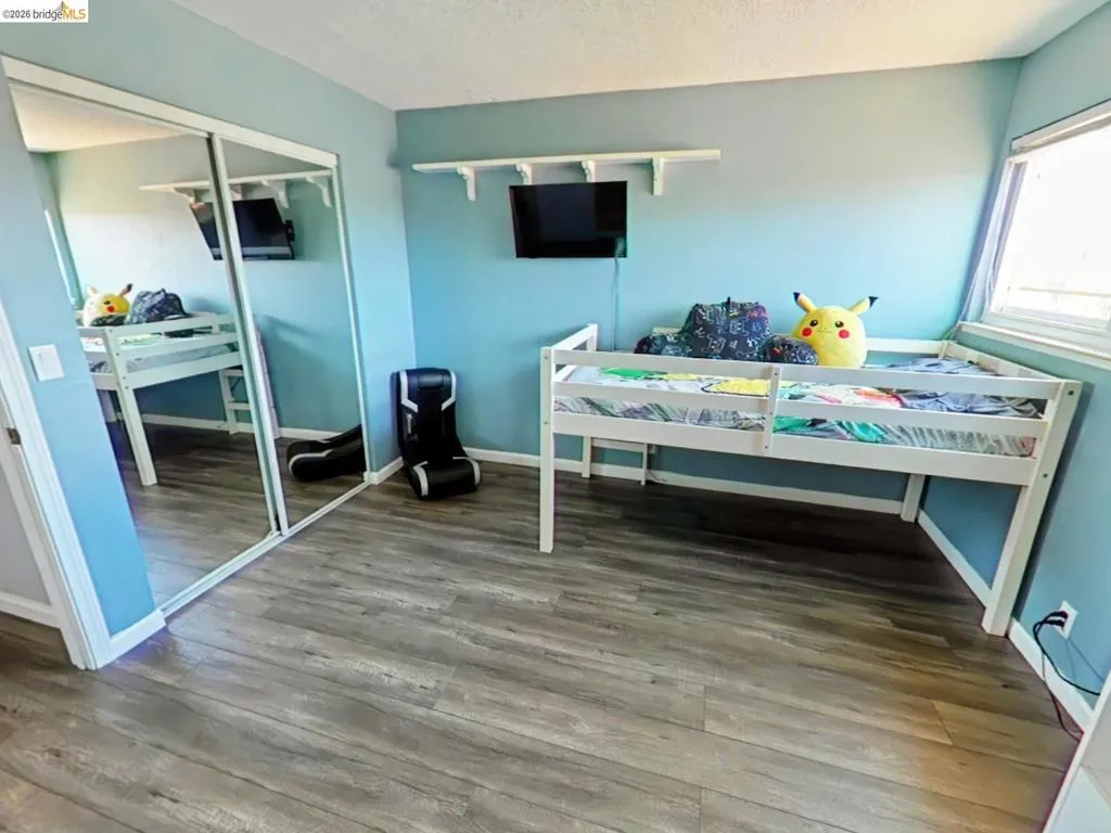 Bedroom featuring wood-finish flooring, a window with blinds, and a mirrored closet with sliding​​‌​​​​‌​​‌‌​​‌​​​‌‌​​​‌​​‌‌​​‌‌​​‌‌​​​​ doors